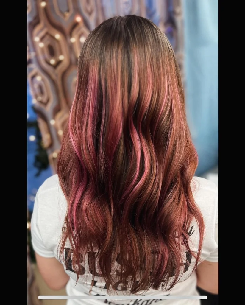 Long wavy hair with auburn base and vibrant pink highlights, professional color at Just Teasin' Salon.