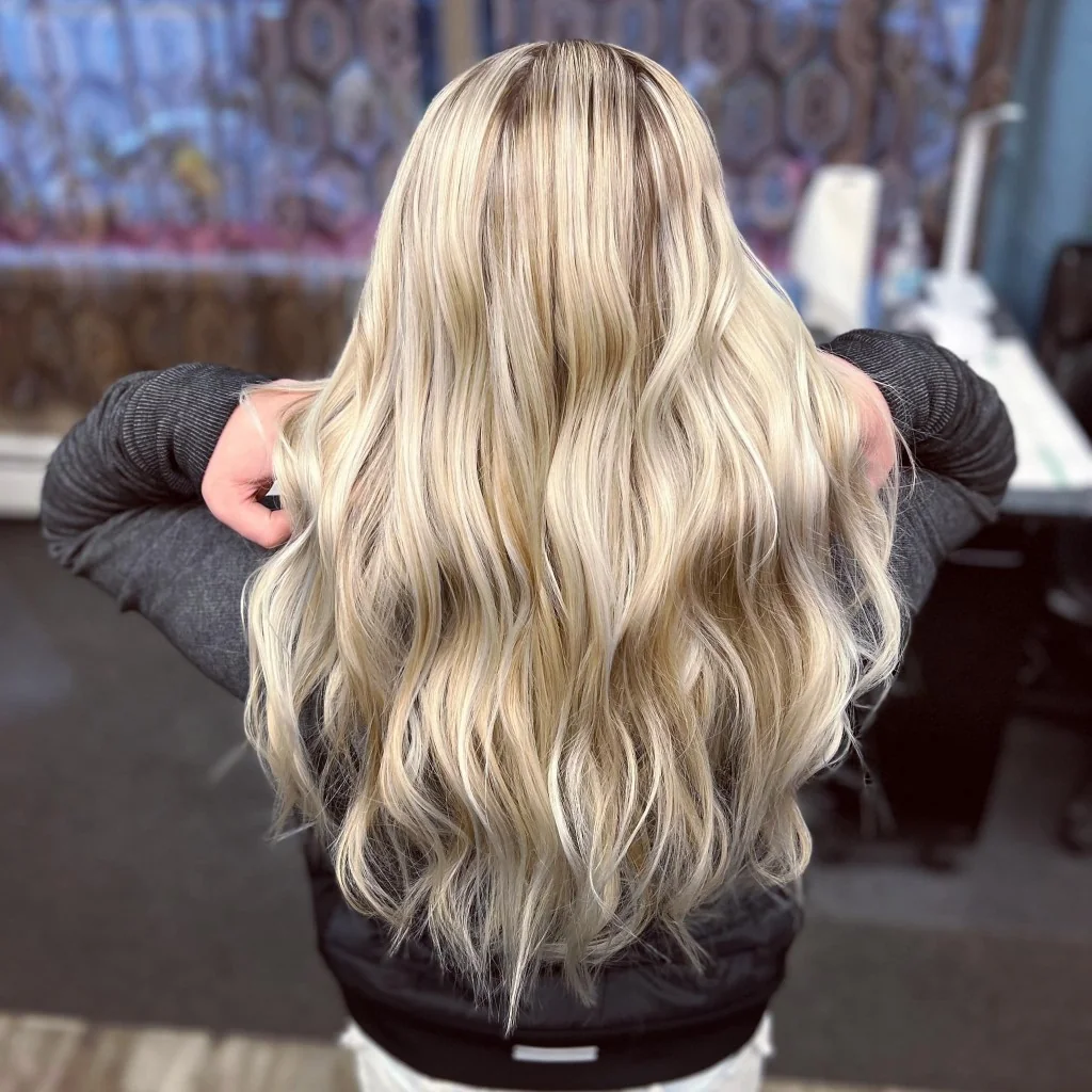 Back view of long wavy hair with cool-toned dimensional blonde highlights at Just Teasin' Salon.