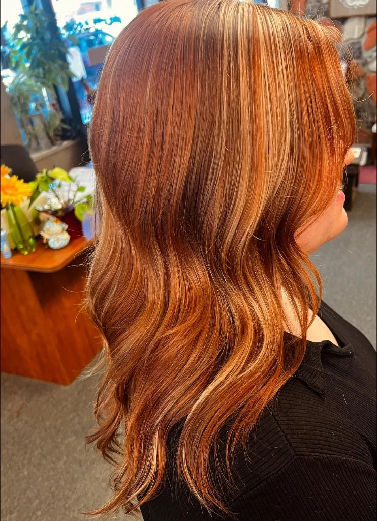 Side profile of long hair with warm copper base and honey-blonde highlights, styled in soft waves.