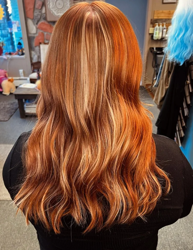 Back view of long wavy hair with copper and blonde ribbon highlights at Just Teasin' Salon, Caro, Michigan.