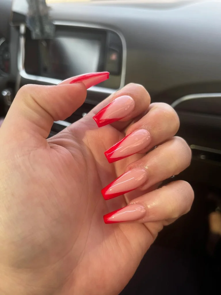 Long coffin nails with nude base and diagonal red French tips in natural daylight.