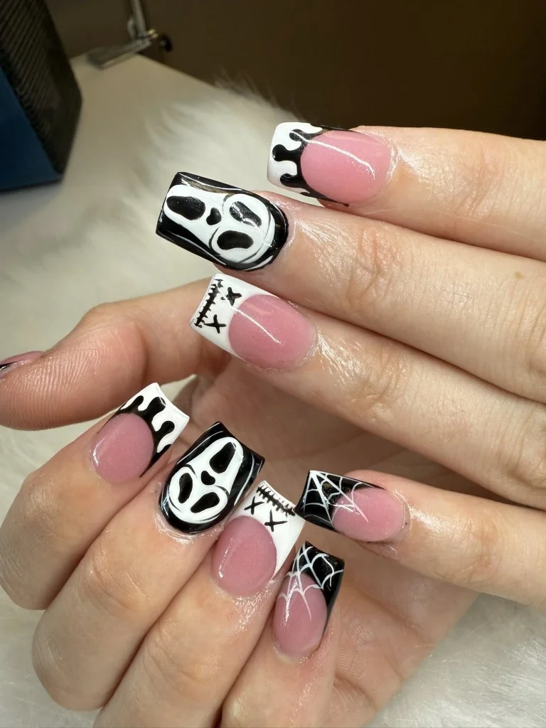 Two hands with long square nails in Halloween-themed black and white nail art on a white fur surface.